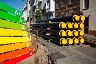 A stack of new pipes for district heating at a construction site, graphic with energy efficiency classes for buildings according to the GEG.